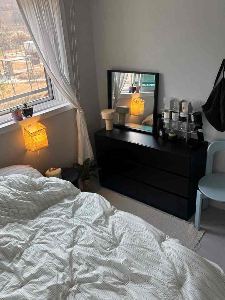 ホワイトとブラックのトーンのワンルーム寝室、ホワイトの寝具とブラックのドレッサー、カーテンが配置された落ち着いた空間