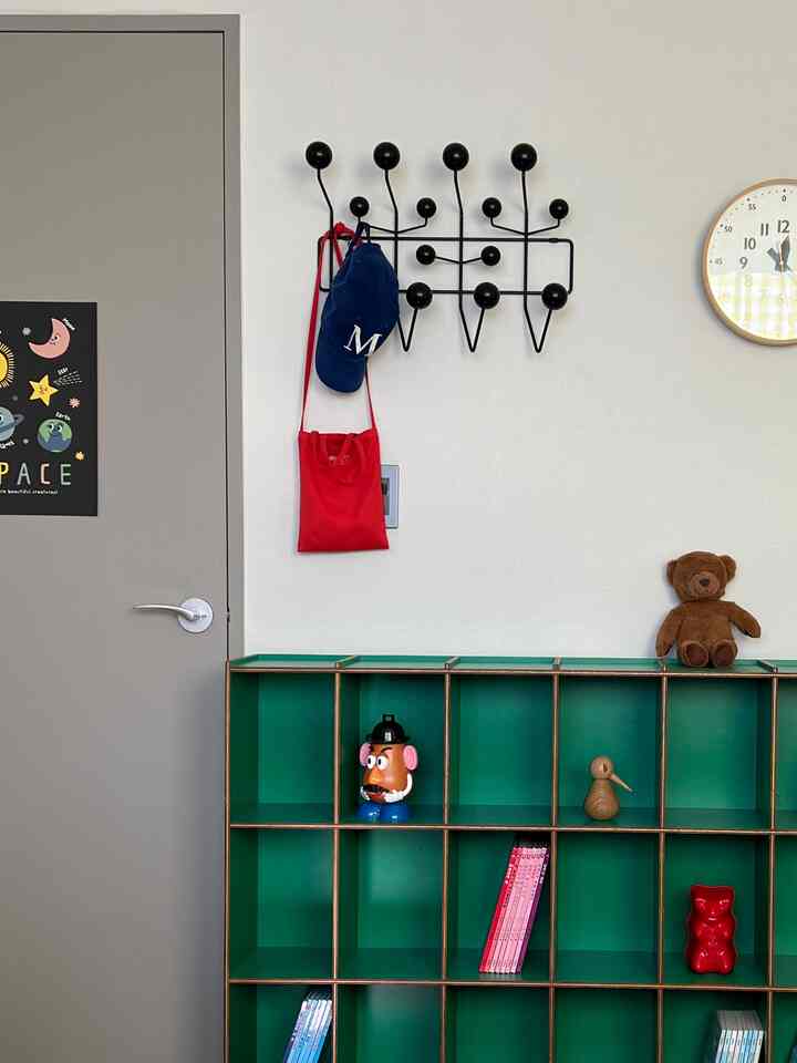 明るい北欧風のインテリア、緑の棚におもちゃが置かれ、壁に黒いフックと時計が配置された空間