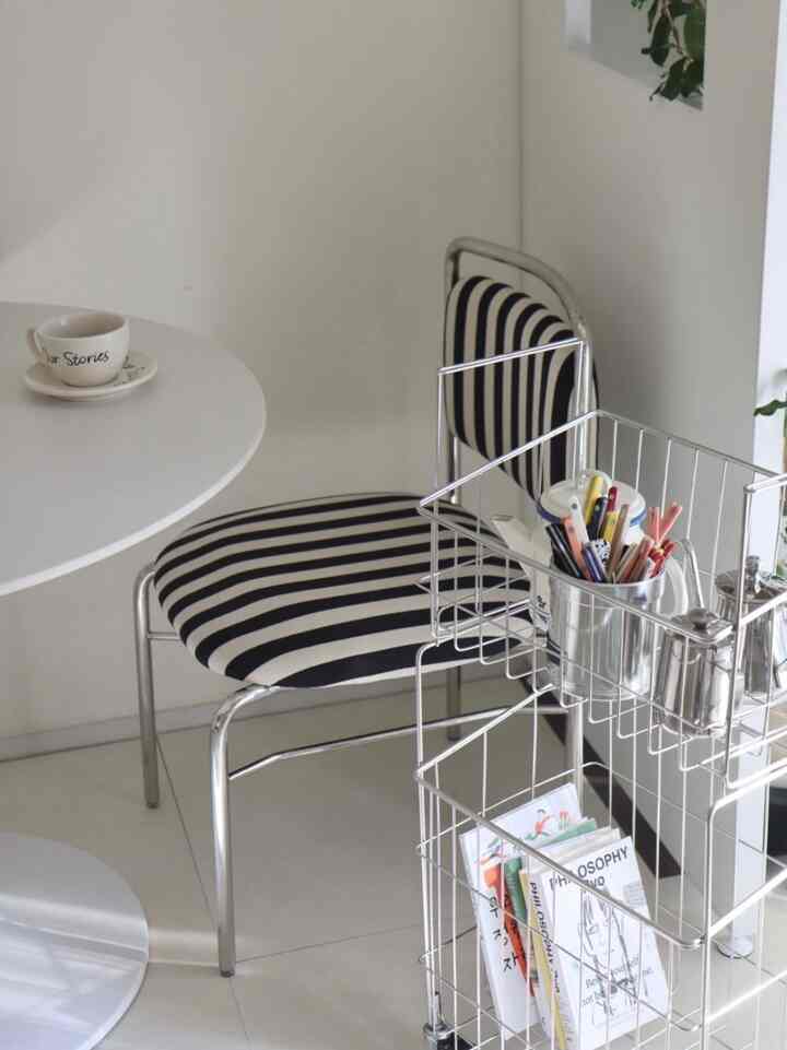 White and silver toned cafe-style dining room featuring striped chairs and metal storage rack in a minimal space
