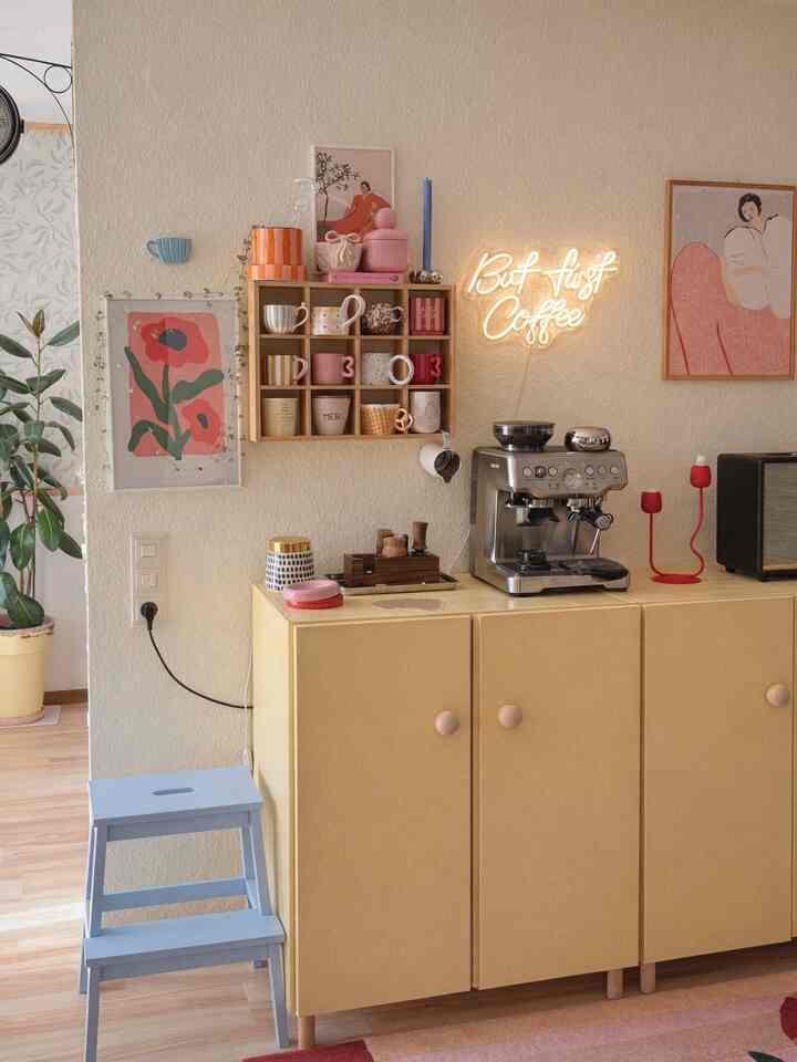 Pastel toned cozy home cafe corner featuring wooden cubby shelf, assorted coffee mugs, and warm neon lighting