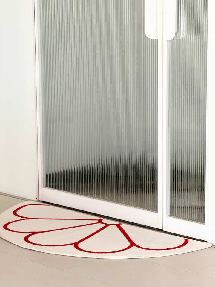 白と赤の模様がある半円形のマットが設置された明るい玄関先のスペース