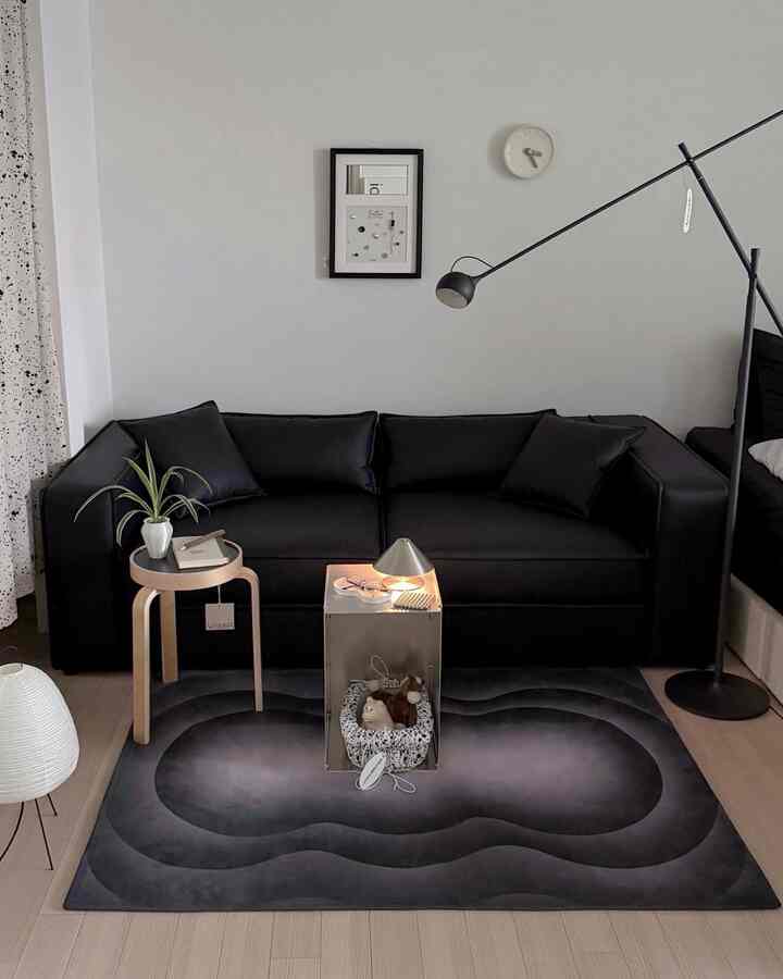モノトーンの黒いリビング、中央に黒のソファとグラデーションのラグが配置された、シンプルで落ち着いた雰囲気のインテリア