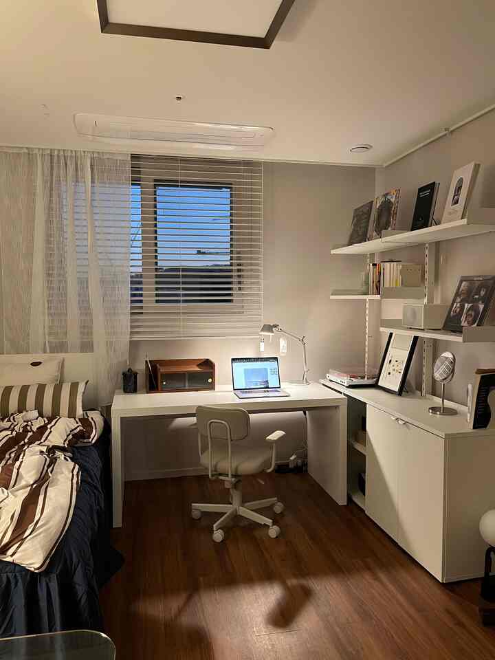 ホワイトとウッド調のモダンなワンルーム寝室、デスクとオフィスチェアが配された清潔感のある空間