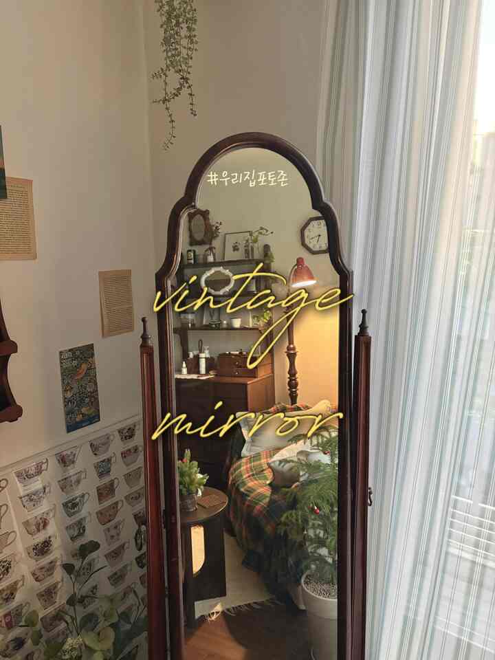 温かみのある木目調とグリーンの植物が調和するヴィンテージ風リビングのフォトゾーン、アンティークミラーと木製家具が配置された落ち着いた空間