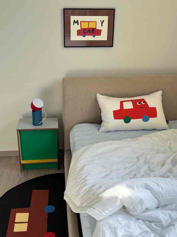 ベージュ色のベッドと白い寝具がある子供部屋、かわいい車柄の枕とポスターが配置された雰囲気のある空間