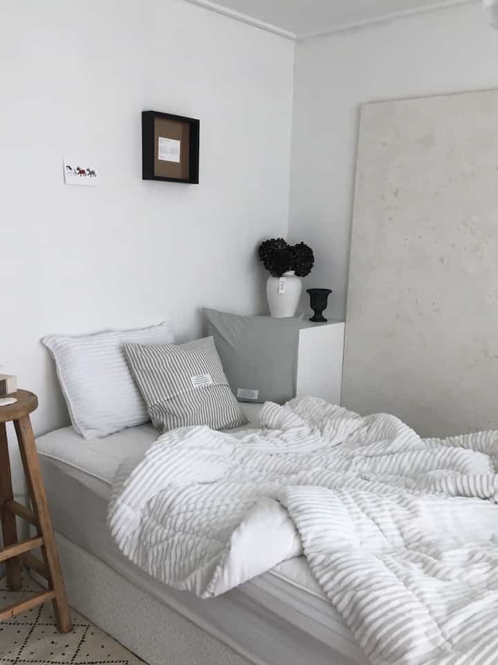 White and gray toned bedroom featuring a neat bed with cushions, creating a modern atmosphere