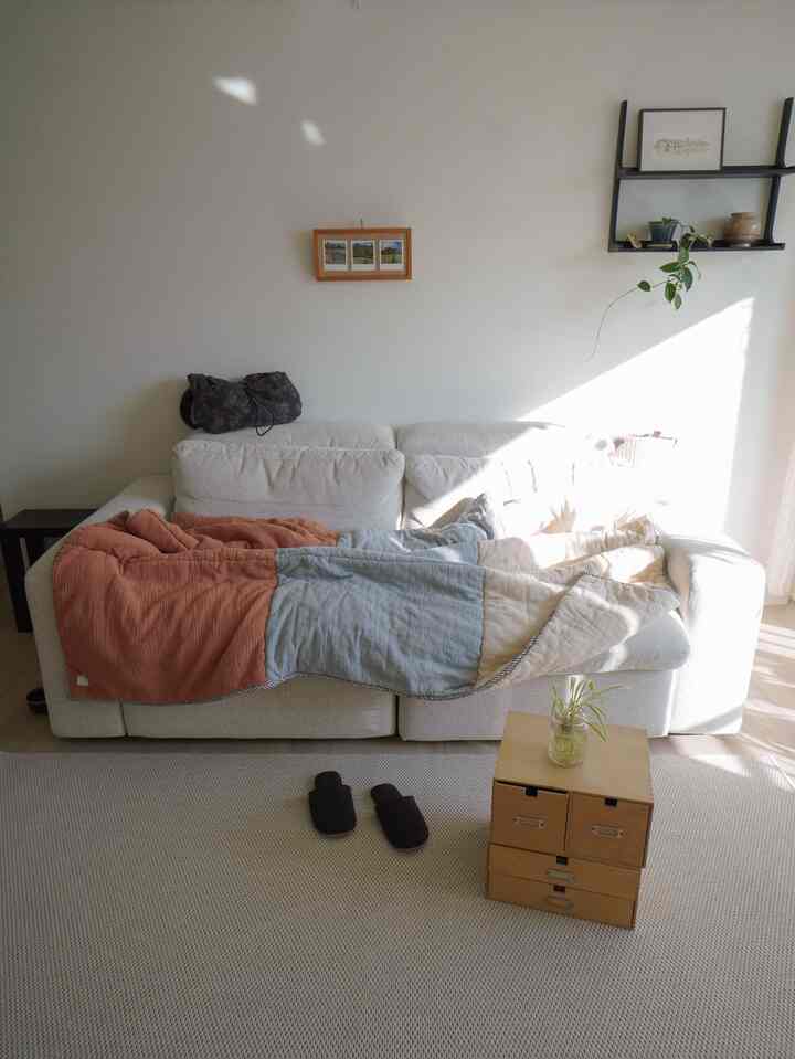 ホワイトとウッドトーンのリビングルーム、快適なソファとラグが配置され、自然光が差し込むシンプルでナチュラルな雰囲気のインテリア