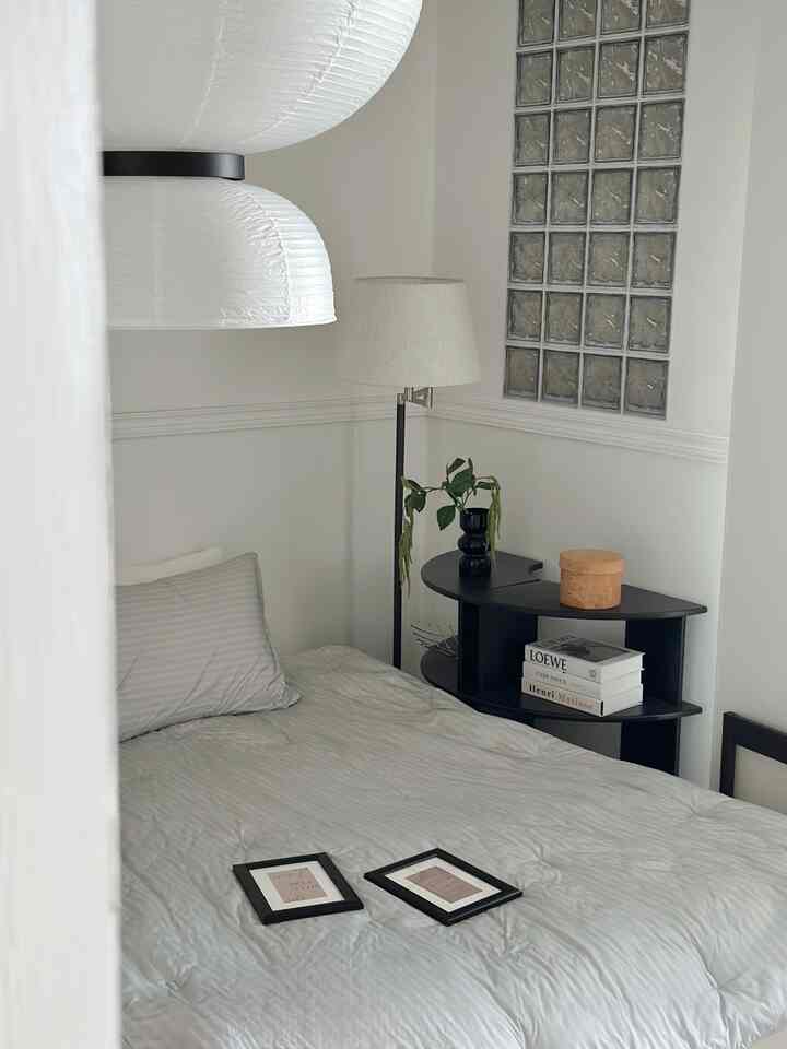 White and black themed bedroom with a nightstand and plant, featuring a natural and serene atmosphere