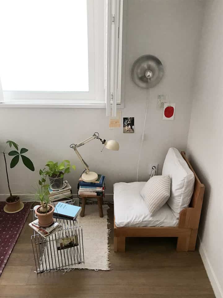 白と木目調の小さな読書コーナー、自然な植物とシンプルな家具が配置された雰囲気のある空間