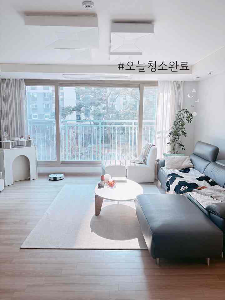 ホワイトトーンのリビング、大きな窓際にソファとアームチェアが配置された清潔で明るい印象的な空間