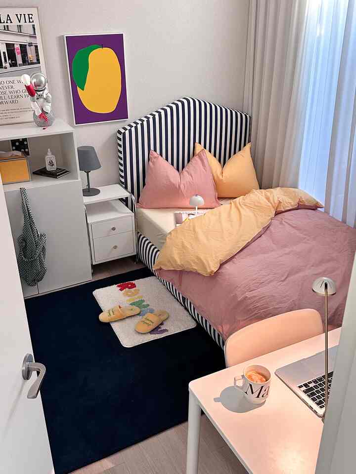 パステル調の寝室、ストライプのベッドフレームとカラフルな寝具、デスクとラグが配置された雰囲気のあるインテリア