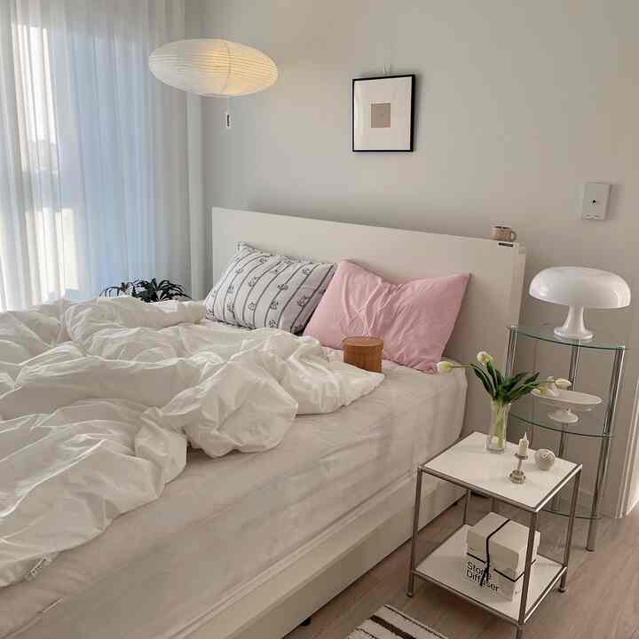 ナチュラルでホワイトトーンの寝室、整ったベッドとナイトテーブル、照明が配置されたシンプルな空間