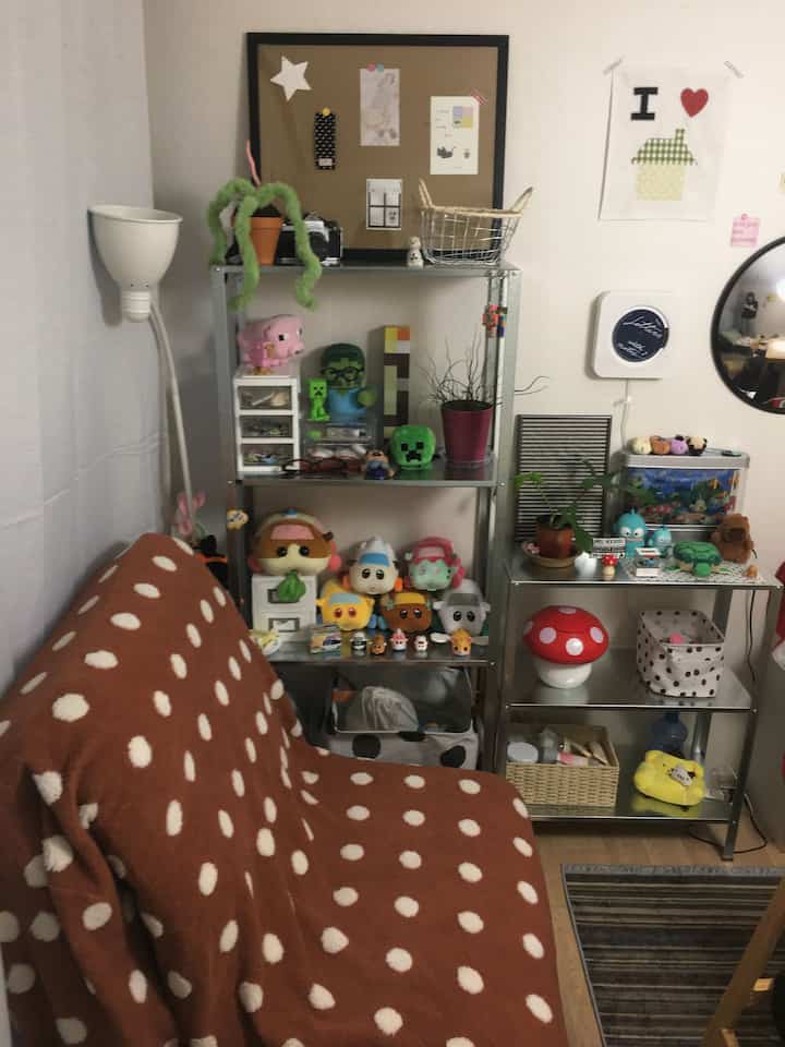 茶色のドット柄ソファとメタルシェルフが置かれた小さな部屋、多様なおもちゃと植物がかわいらしく配置された居心地の良い空間