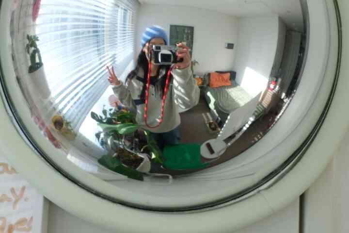 明るいホワイトとウッドトーンの6畳ワンルーム、凸面鏡とグリーン植物、ダイニングチェアが配置された暖かみのある空間