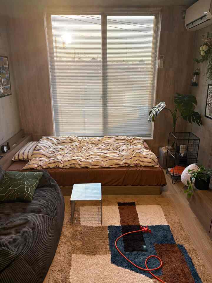 暖かいナチュラルカラーの1Kスタジオ、ベッドとビーズクッションソファ、幾何学模様のラグが配置された印象的な空間