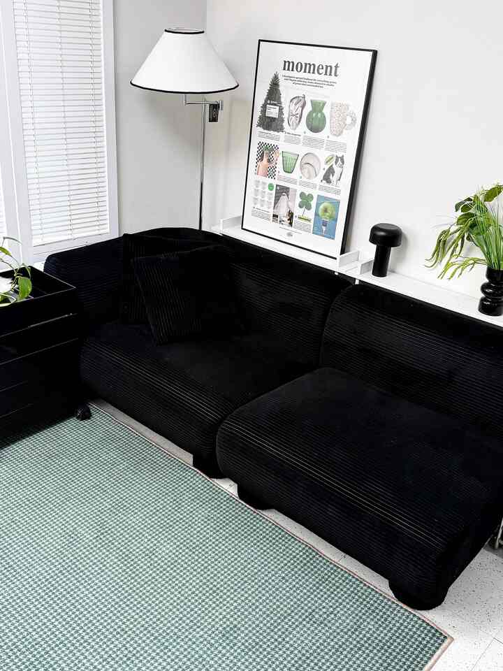 ブラックのソファとホワイトのフロアランプ、額縁が配置されたシンプルなリビングスペース