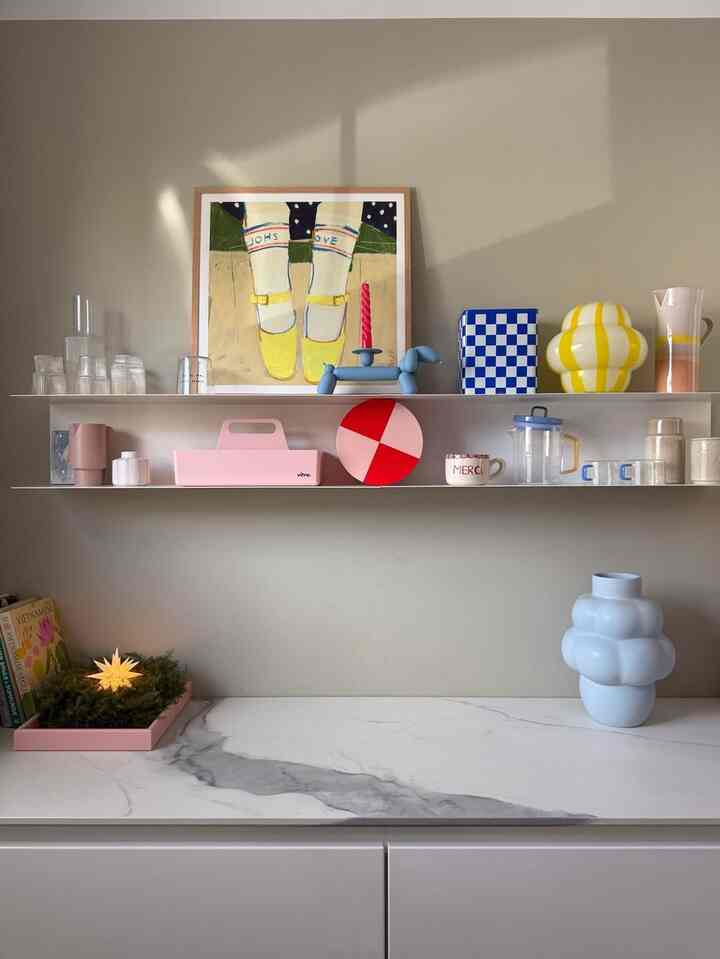 Warm beige toned space with white shelves showcasing colorful decor and modern objets blending playful style