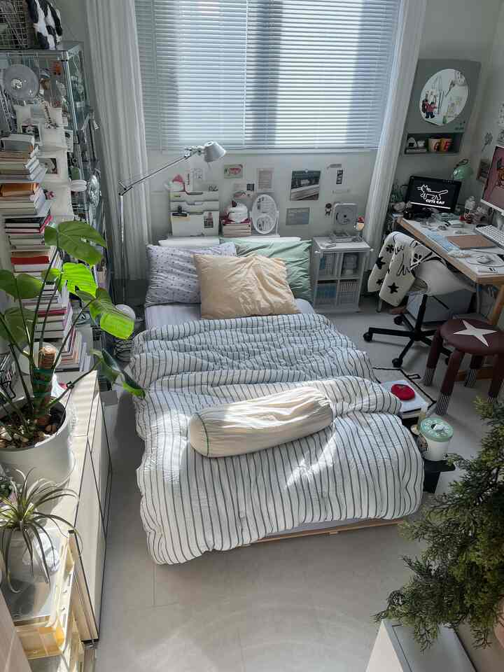 ホワイトとナチュラルトーンの寝室兼ホームオフィス、ブラインドと植物が配置された雰囲気のあるインテリア