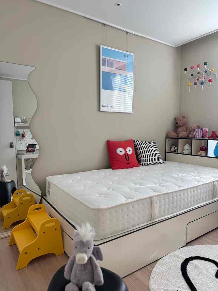 ナチュラルカラーの子供部屋、ベッドと黄色い子供用スツール、多彩な壁飾りが配置された雰囲気のあるインテリア