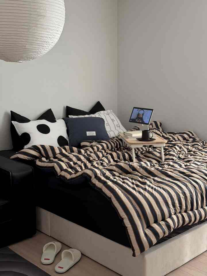 Natural beige and black bedroom featuring a bed with striped bedding, foldable bed table, and slippers creating a cozy atmosphere