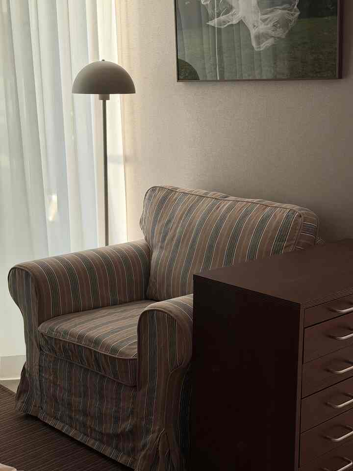 暖かいブラウンとベージュの寝室コーナー、ヴィンテージストライプのアームチェアとフロアランプが配置された落ち着いたインテリア