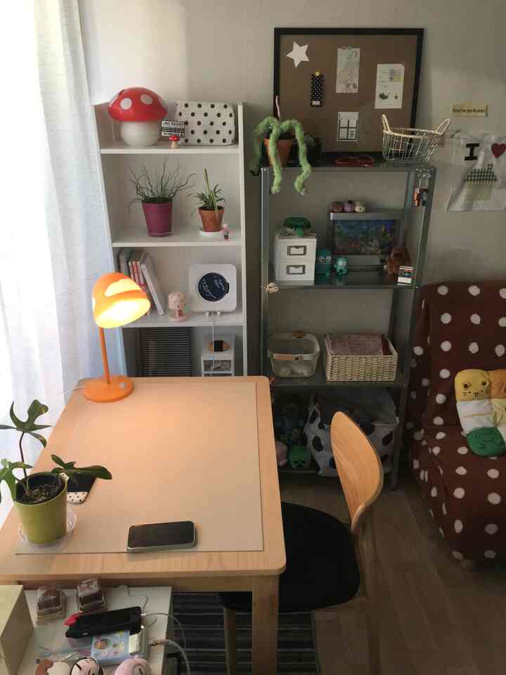 ナチュラルな色調の小さな部屋、木製のダイニングテーブルと本棚、温かみのある照明が配置された雰囲気のあるインテリア