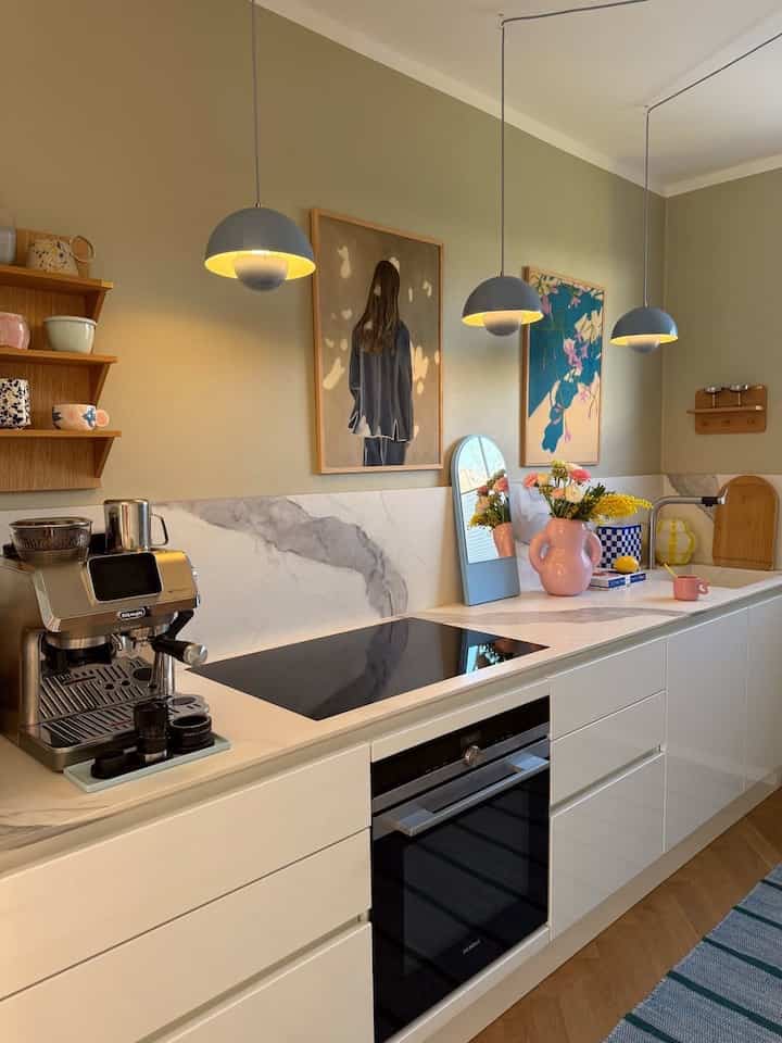 Warm beige walls and white marble countertop in a modern Scandinavian kitchen, featuring a coffee machine and artistic decor elements