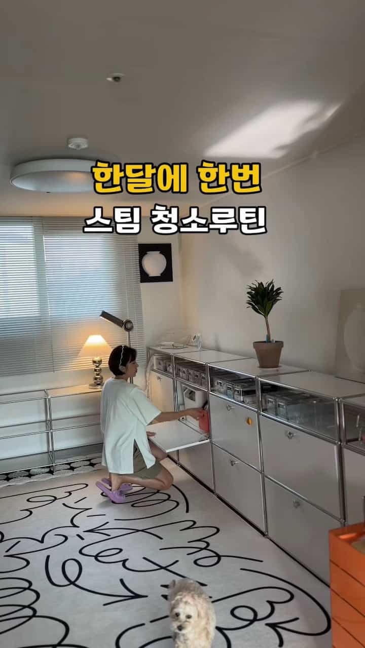 ホワイトとモダンな色調のリビング、金属製収納棚と大きな白いラグが配置された印象的な空間