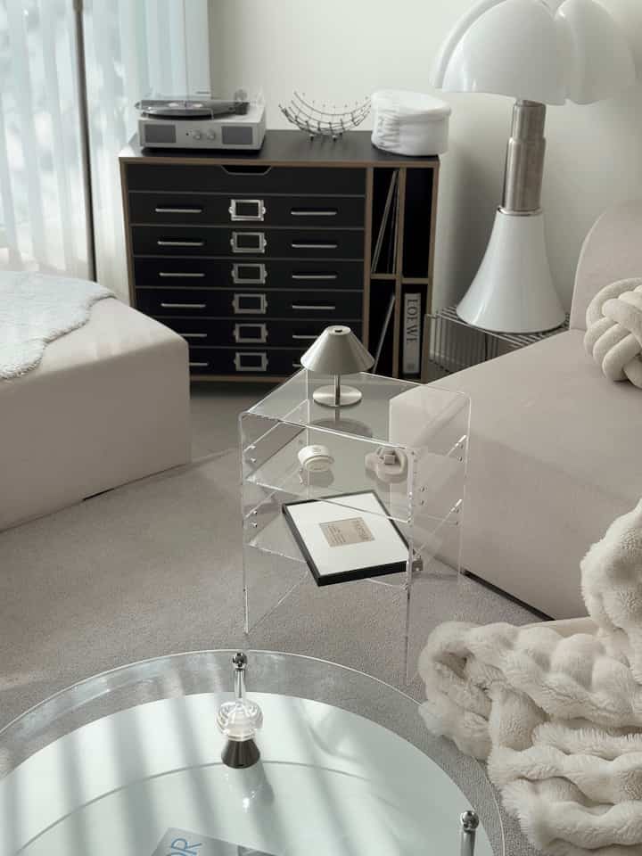 透明なアクリルサイドテーブルとベージュのソファが配置されたモダンでミニマルなリビングスペース