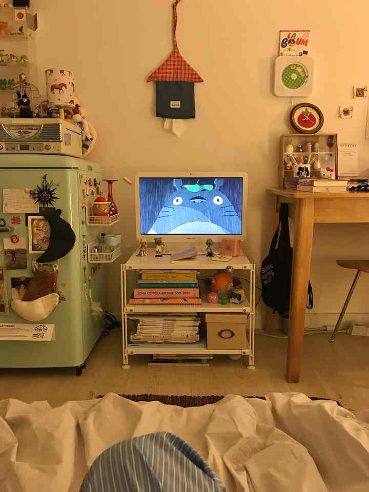 ベージュの色調の寝室空間、緑のレトロなミニ冷蔵庫とモニターが配置されたナチュラルモダンなインテリア