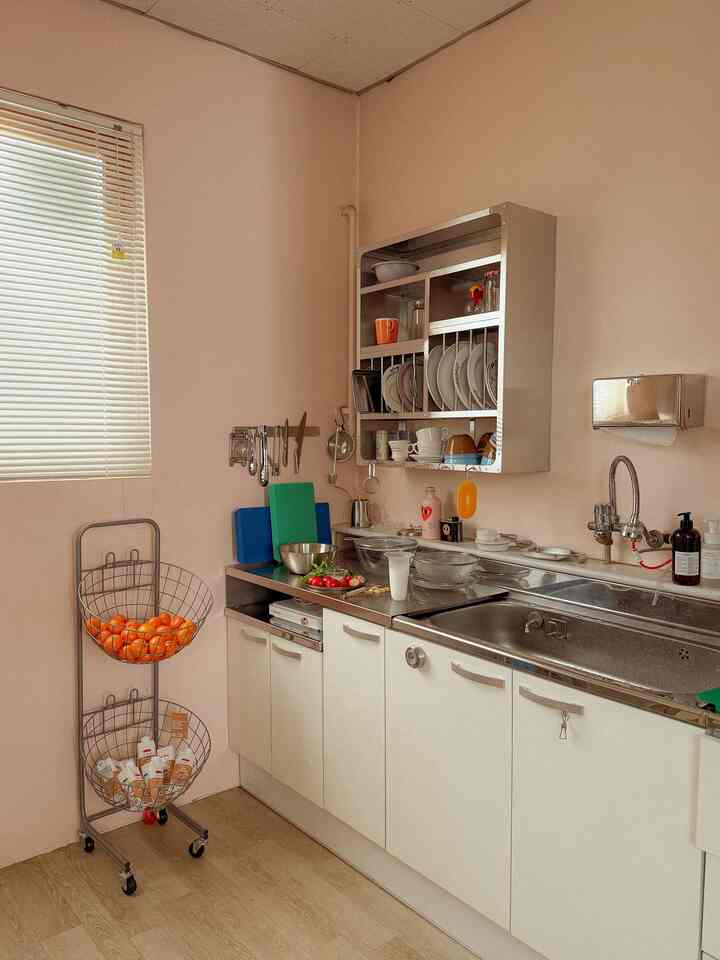Compact kitchen space with soft white and wood tones, featuring wall-mounted dish rack and mobile basket cart for charming practical interior