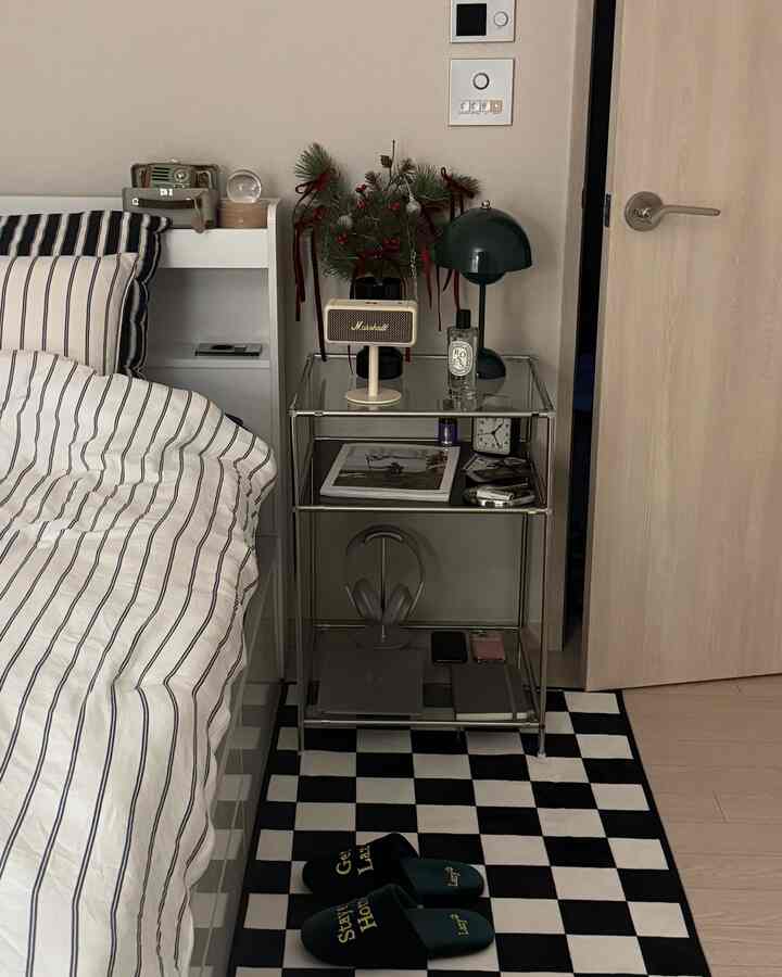 Black and white tone bedroom featuring bed, shelving unit, and a glass nightstand with decorative objects creating a chic and warm atmosphere