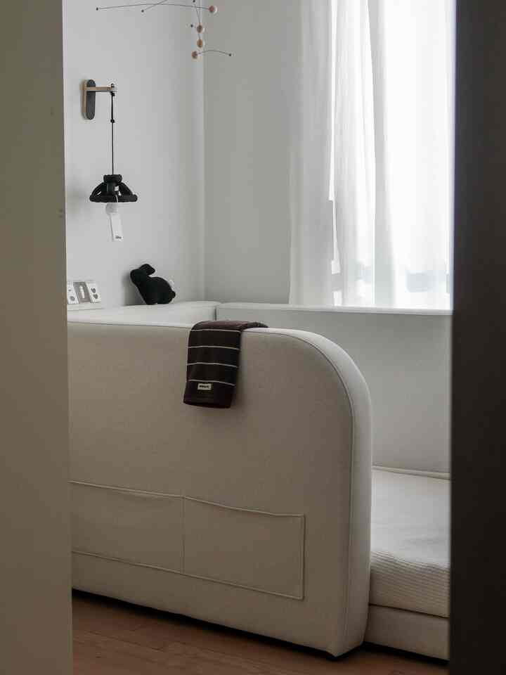 白とナチュラルな色調の赤ちゃん部屋、デイベッドと安全ガードが配置された印象的な空間