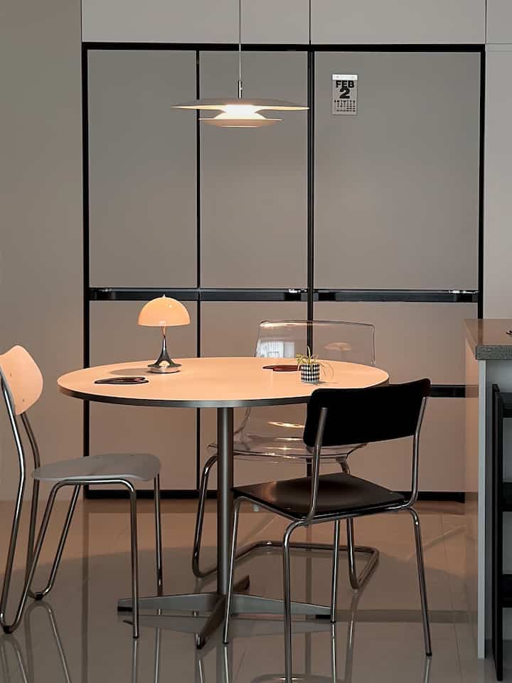 白とシルバーのトーンのダイニング、丸いダイニングテーブルと多様な椅子が配置されたモダンで清潔感のあるインテリア