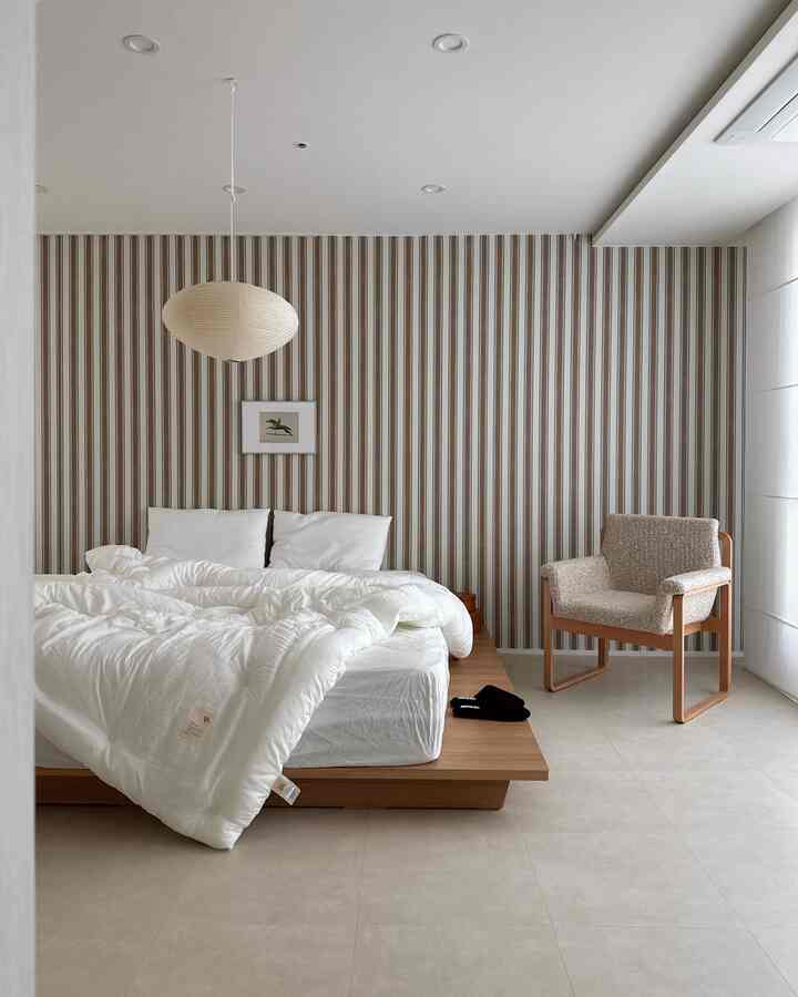 ホワイトと木目調が調和したミニマルモダンなロータイプベッドの寝室、快適なアームチェアを備える