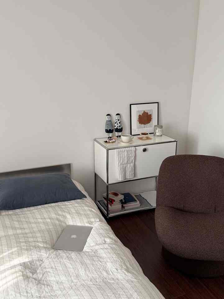 白とダークブラウンの色調の寝室、ベッドとナイトテーブル、ブラウンのアームチェアが配置されたミニマルな雰囲気のインテリア