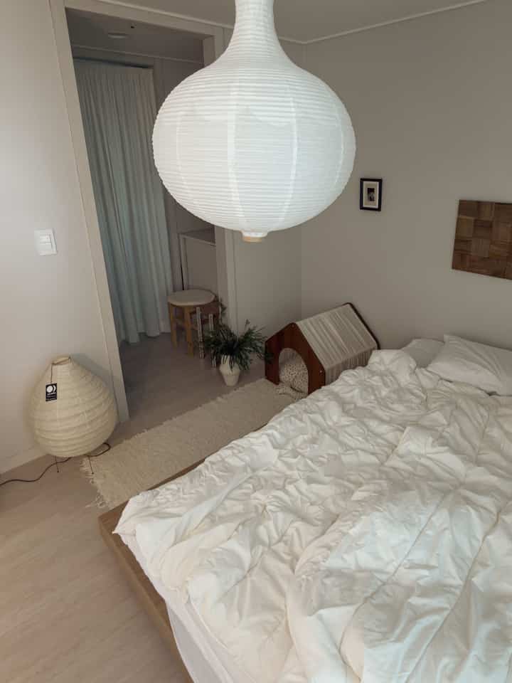 白とナチュラルな色調の寝室、心地よいベッドとペットハウスが配置された印象的で落ち着いたインテリア