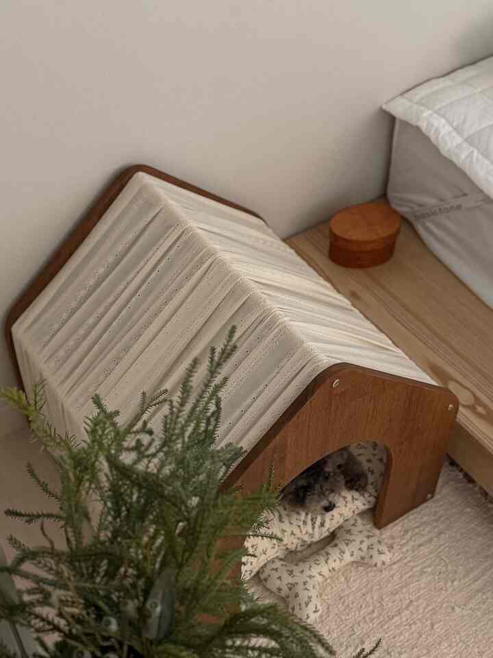 ナチュラルな色調の寝室の一角に、木製のペットハウスとクッションが配置された雰囲気のある空間