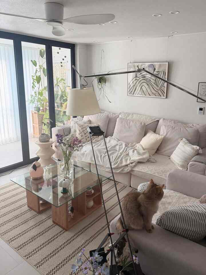 ナチュラルなベージュとホワイトの色調のリビング、広いコーナーソファとガラステーブルが配置された落ち着いた空間