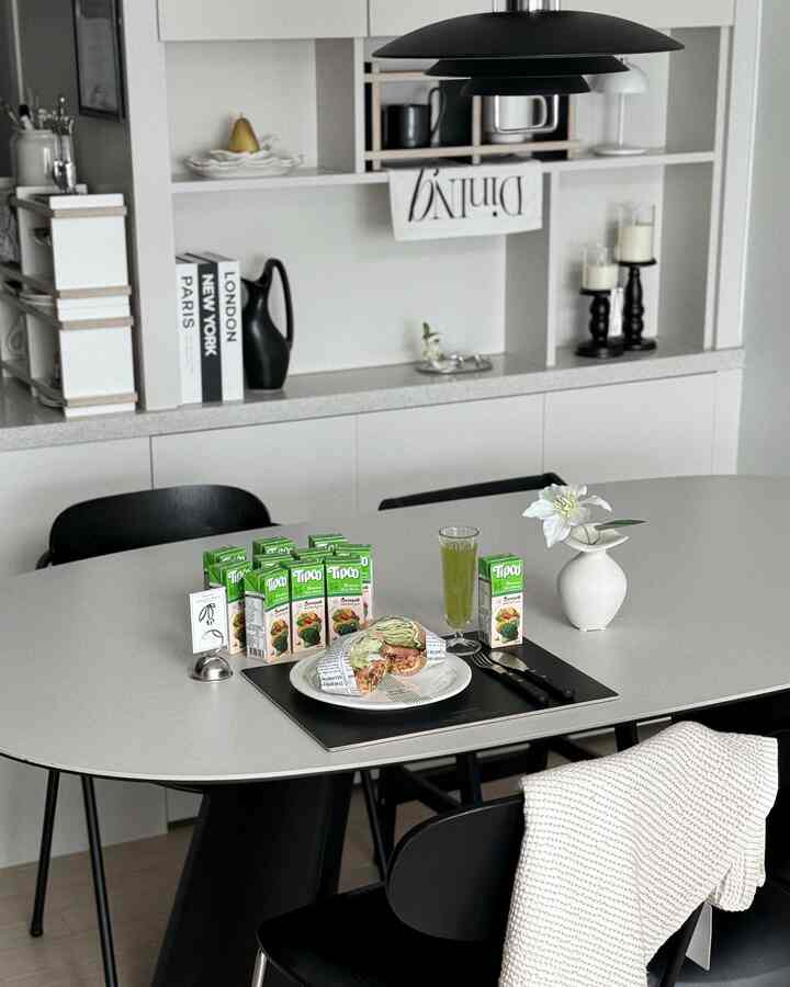 白と黒のモダンなダイニングルーム、中央に白いダイニングテーブルと黒い椅子、ブランチのプレートとティプコのジュースが配置された印象的な空間