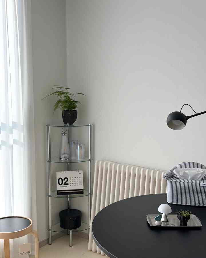 白を基調としたモダンなリビングのコーナーに黒い丸テーブルとガラスのコーナー収納が配置された、清潔感のあるインテリア