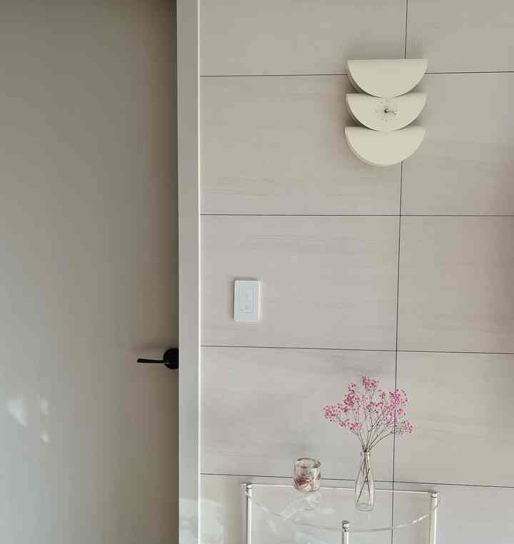 ベージュ色調の玄関空間、透明な棚と洗練された壁時計が配置されたミニマルで清潔感のあるインテリア