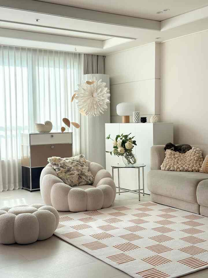 ナチュラルカラーのリビング、ベージュのソファとスツール、チェック柄のラグ、透明な花瓶が配置された雰囲気のある空間