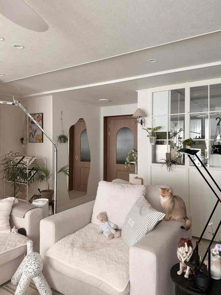 温かみのあるベージュとホワイトのトーンのリビング、一人掛けソファと猫、照明やオブジェが配置された雰囲気のあるインテリア