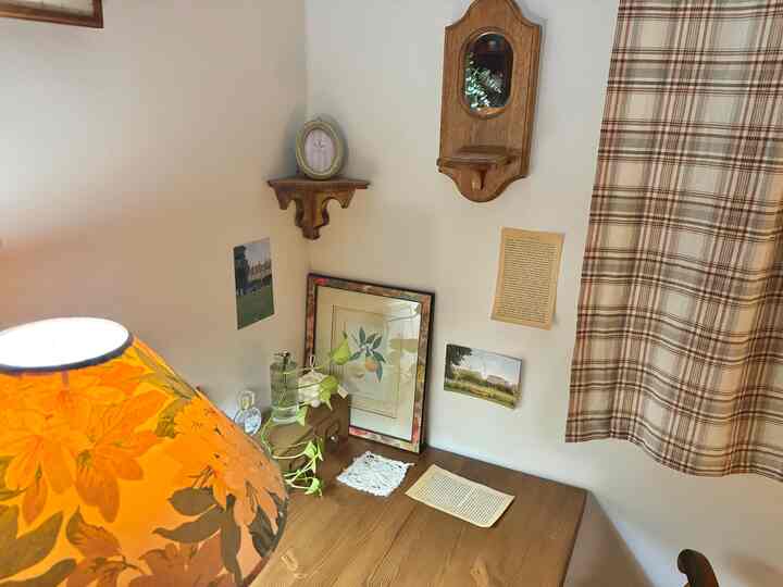 ナチュラルな色調の小さな空間、木製の棚と壁掛け鏡、花柄のテーブルランプが配置された雰囲気のあるコーナー