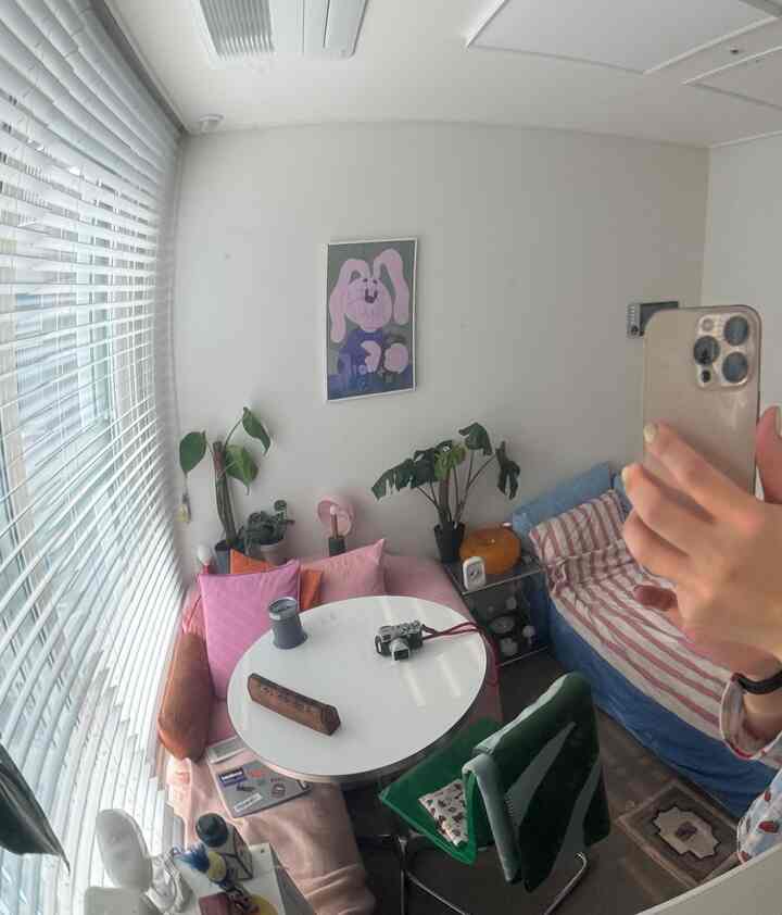 白とパステル調のワンルーム、丸いダイニングテーブルと椅子、クッション、植物が配置された雰囲気のあるインテリア