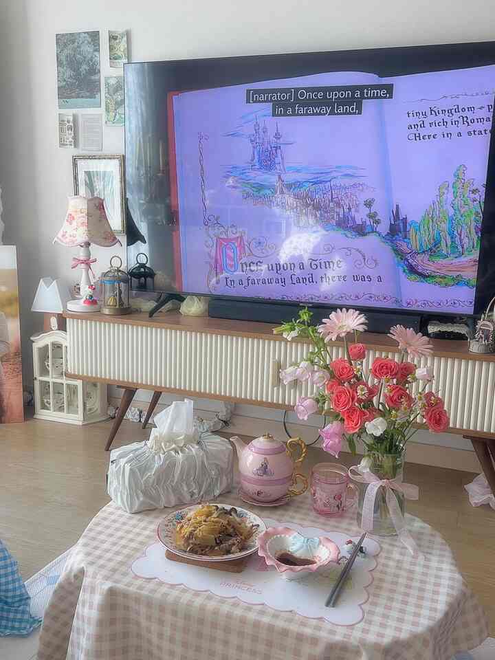 ピンクのヴィンテージ調リビング、ディズニープリンセスのティーカップとティーポット、花が置かれた印象的なホームカフェの空間