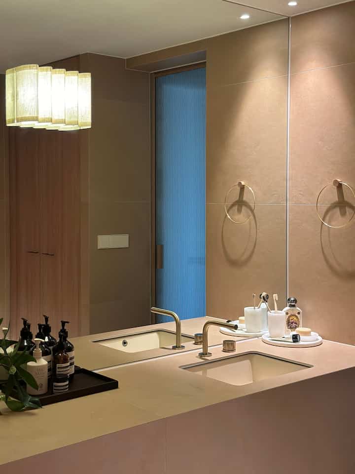 ベージュの色調のバスルーム洗面台、ゴールドの蛇口と丸いタオル掛けが配置された清潔で現代的なインテリア