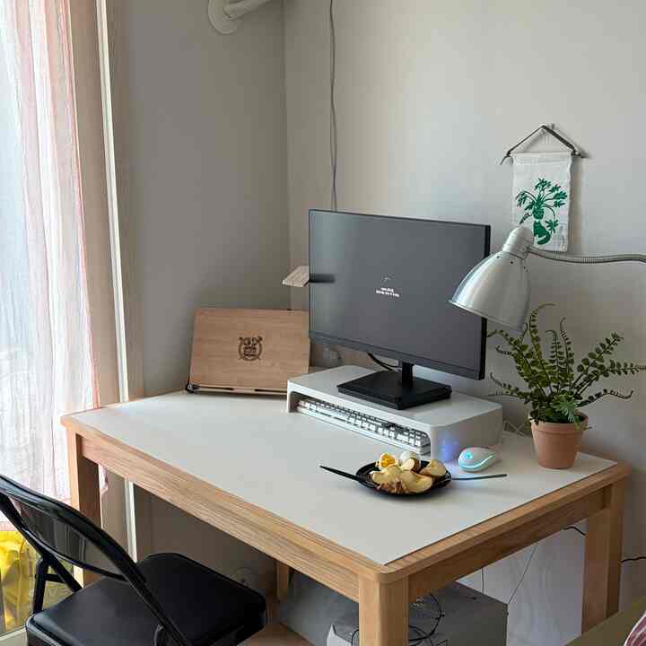 白い壁と木目調のデスクが配置された清潔感のあるホームオフィス、モニターとフロアランプが特徴的な空間