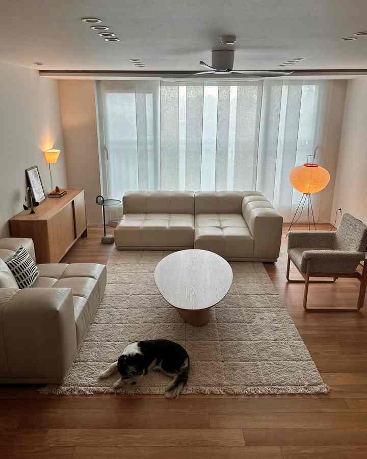 ナチュラルな色調のリビングルーム、ベージュのラグとレザーソファ、木製家具、温かみのある照明が配置された雰囲気のあるインテリア